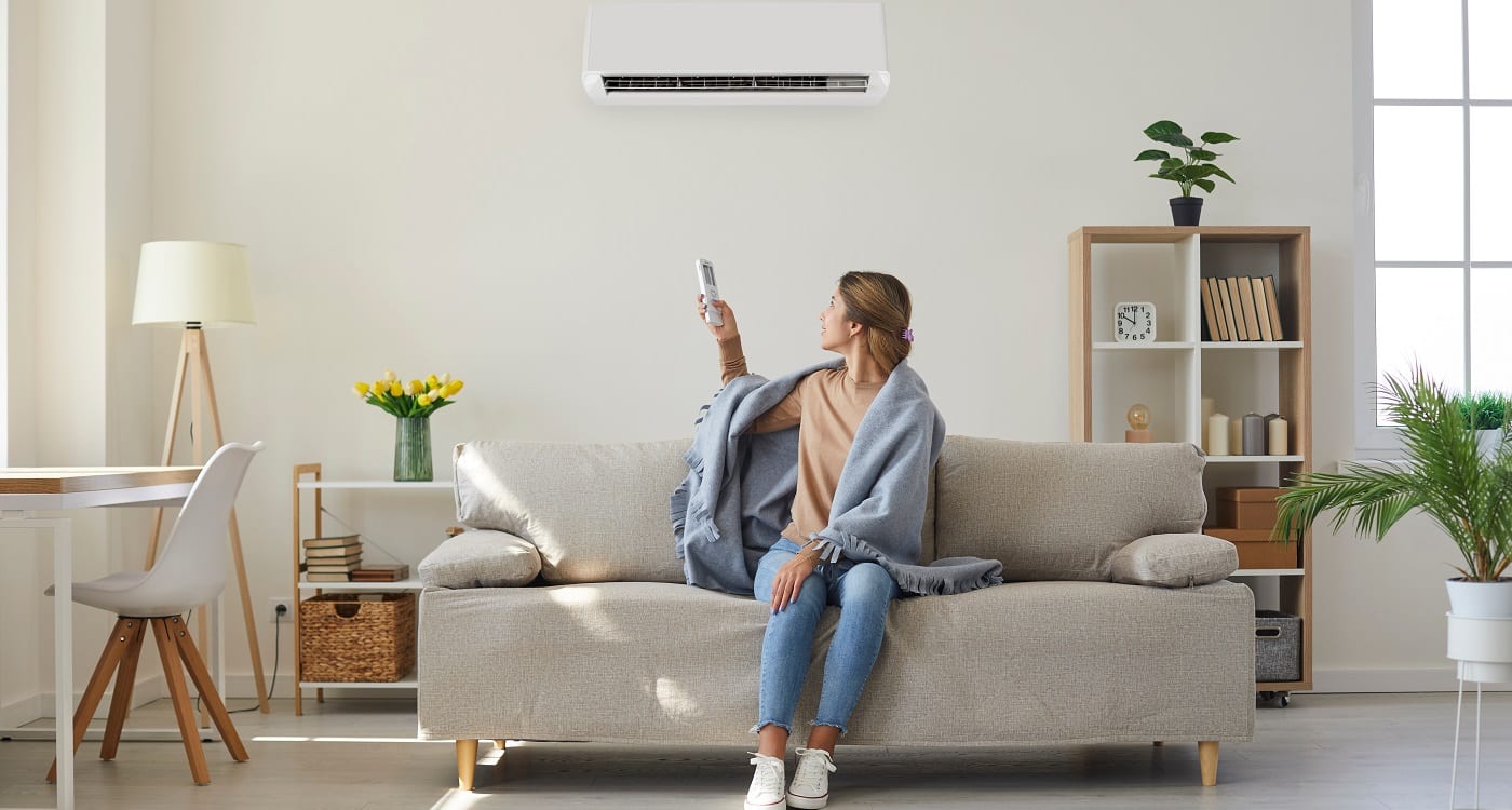 Dame sitzt im Wohnzimmer Ihres Einfamilienhauses und schaltet mit einer Fernbedienung Ihre Klimaanlage an